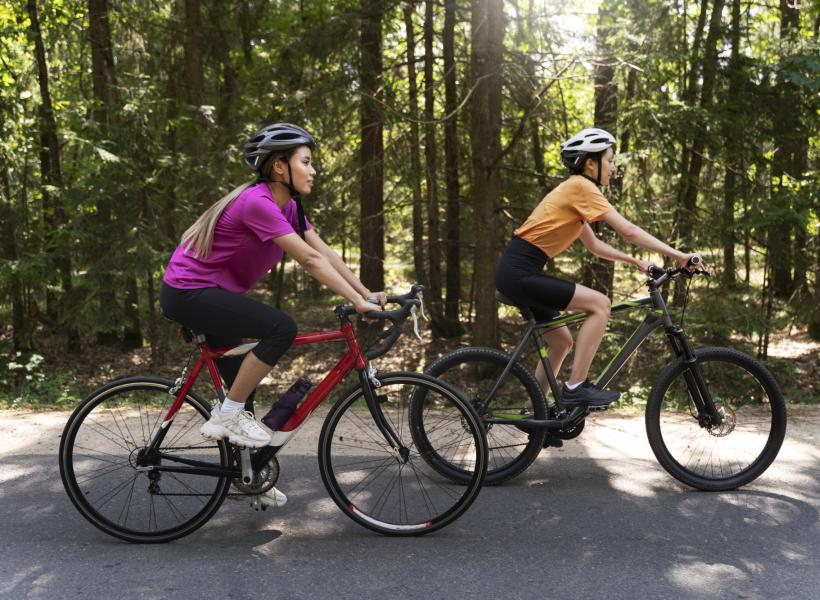 Two cyclists ride bikes on a road through the forest.