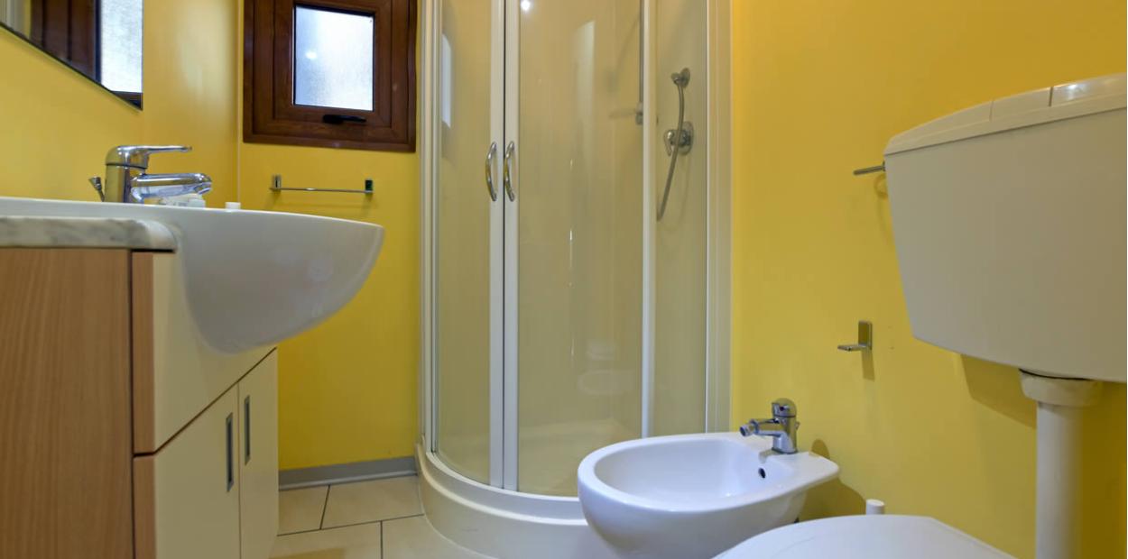 Bagno con doccia angolare, lavandino, bidet e pareti gialle.