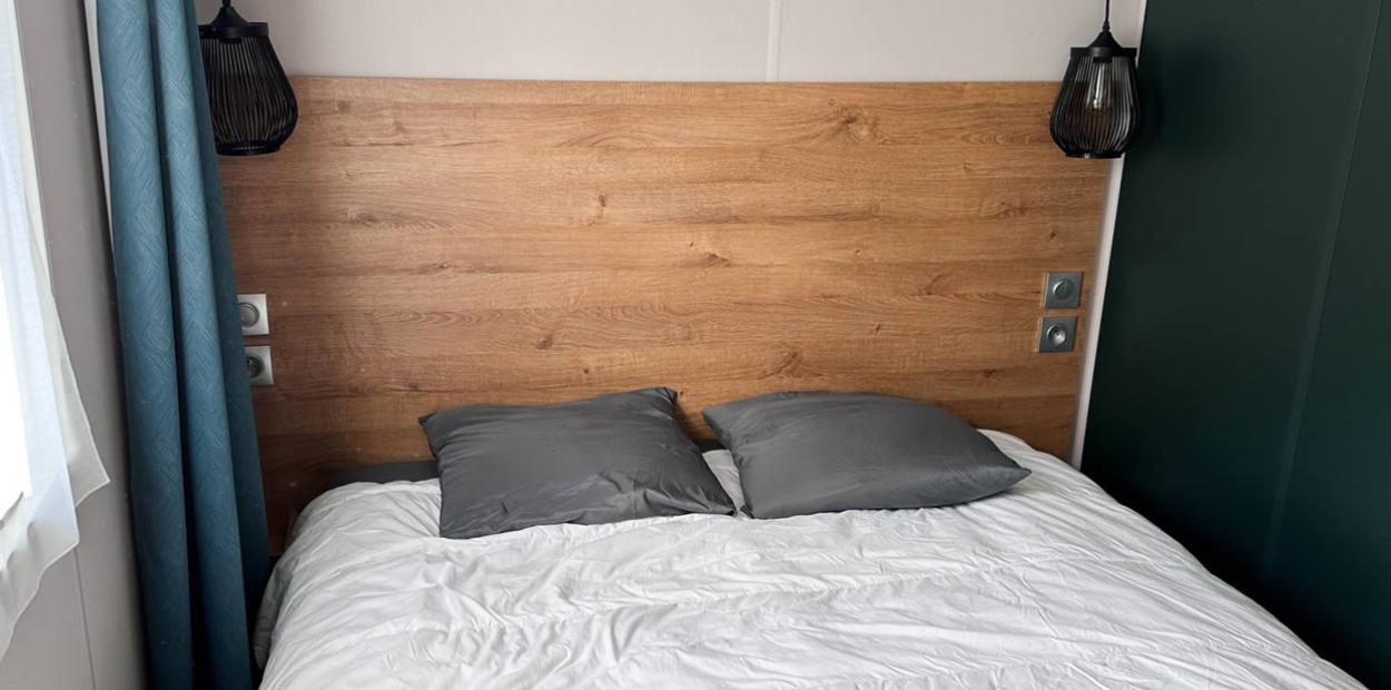 Camera da letto con testiera in legno, cuscini grigi e lampade moderne.