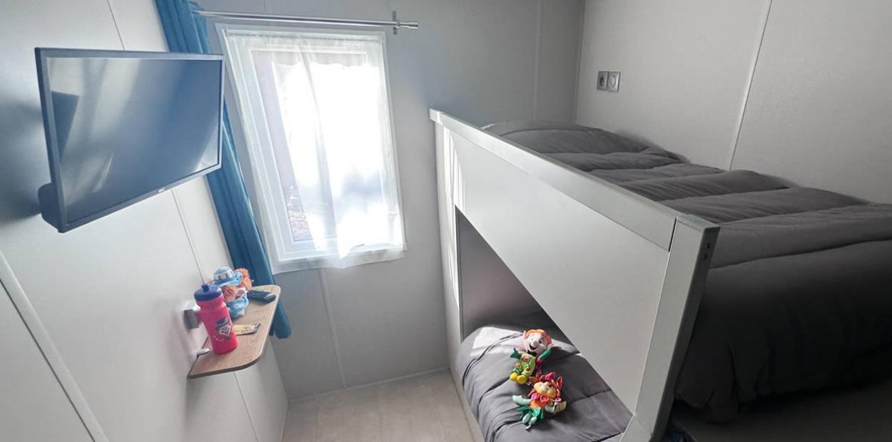 Camera con letto a castello, TV, peluche e finestra con tenda bianca.