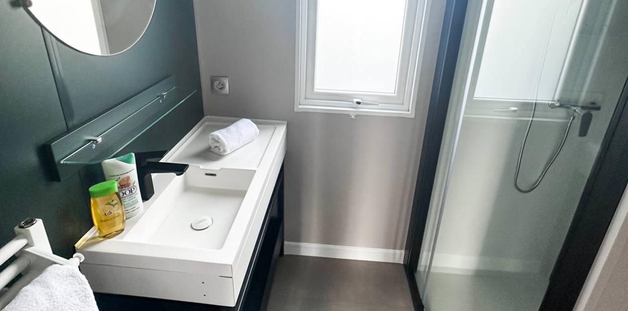 Bagno moderno con doccia, lavabo bianco, specchio rotondo e finestra.