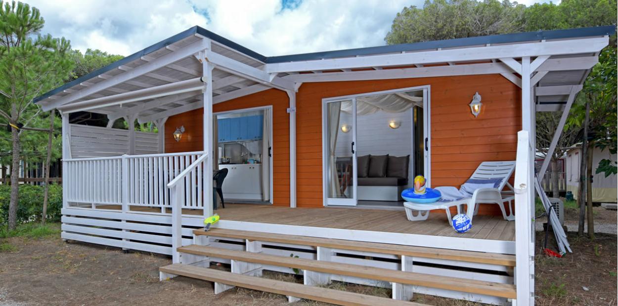 Bungalow in legno con veranda, sedie a sdraio e giochi per bambini.
