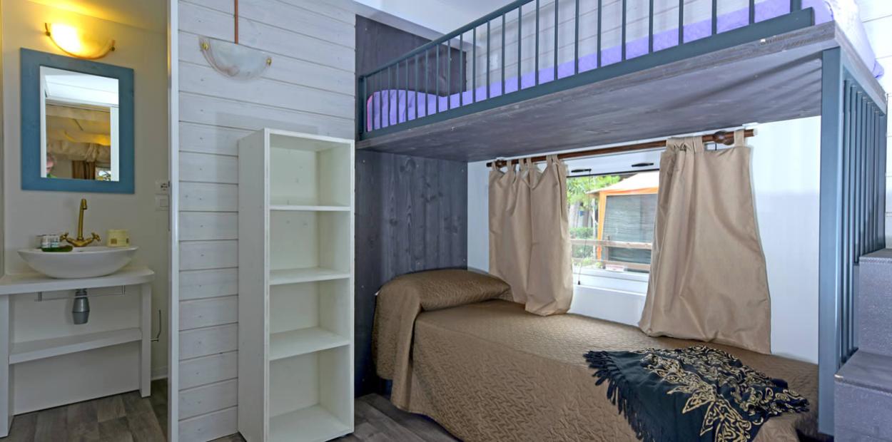 Camera con letto a castello, scaffale bianco e lavabo con specchio azzurro.