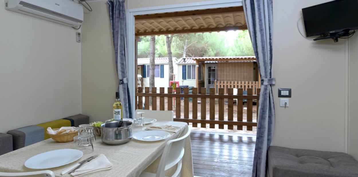 Interno di una casa mobile con tavolo apparecchiato e vista sul patio esterno.