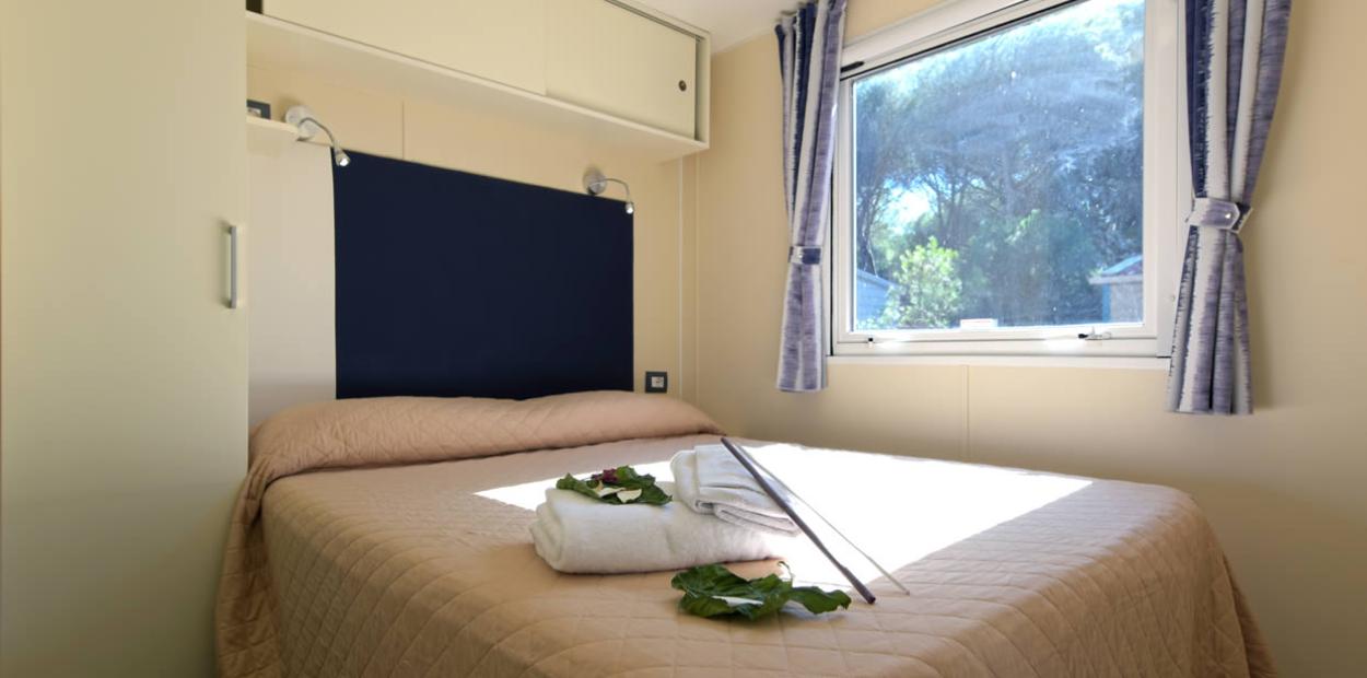 Camera luminosa con letto matrimoniale, finestra ampia e asciugamani piegati sul letto.