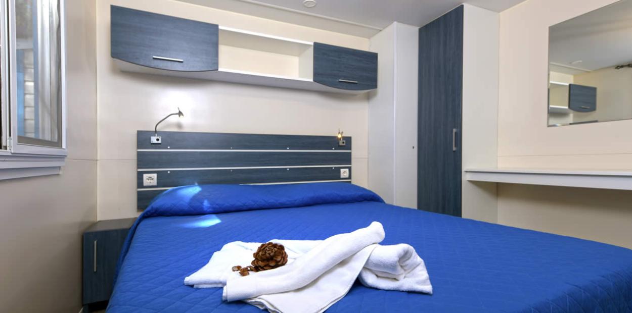 Camera moderna con letto matrimoniale e arredi blu, asciugamani piegati sul letto.
