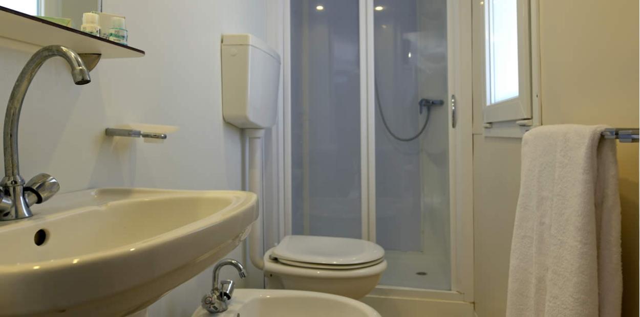Bagno compatto con lavabo, bidet, WC, doccia e asciugamano appeso.