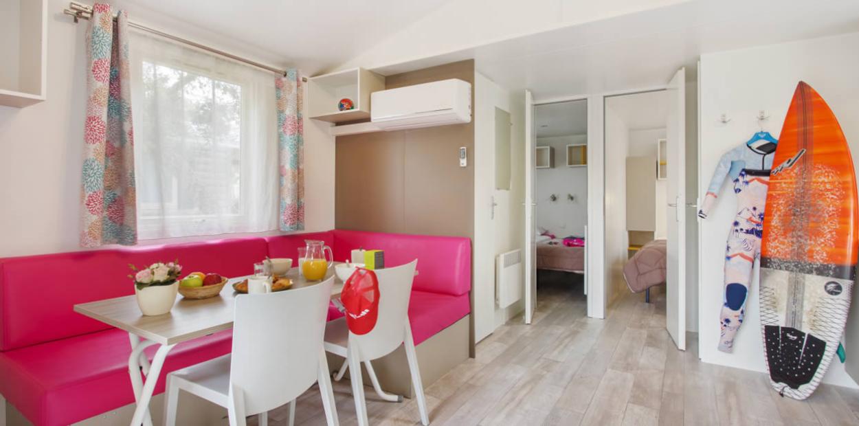 Interno moderno con tavolo apparecchiato, divano rosa, tavola da surf e muta appesa.