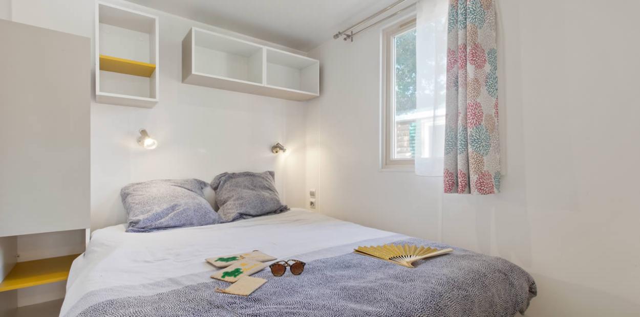 Camera da letto luminosa con letto matrimoniale, mensole e decorazioni semplici.