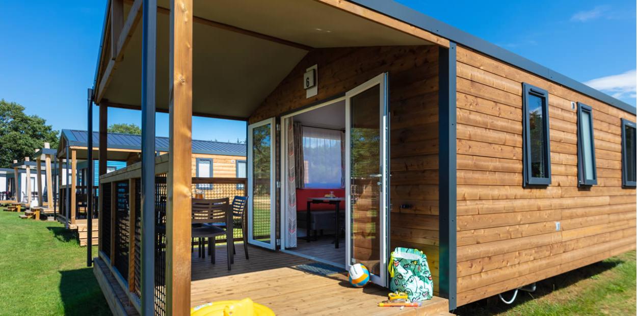 Bungalow in legno con veranda, arredamento estivo e ampio spazio verde.