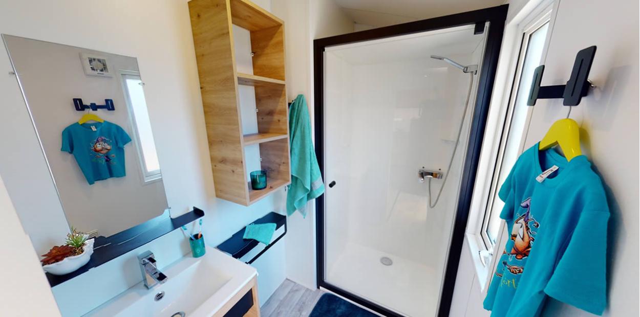 Bagno moderno con doccia, specchio, scaffale in legno e maglietta appesa.
