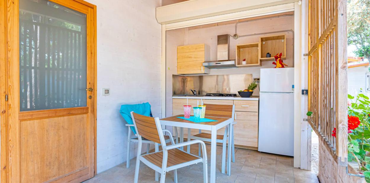 Cucina all'aperto con tavolo, sedie, frigorifero e decorazioni colorate.
