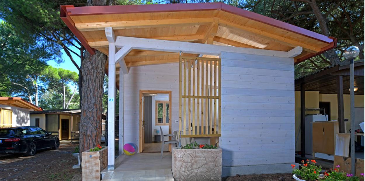 Piccola casetta in legno con veranda, immersa tra gli alberi, decorata con fiori.