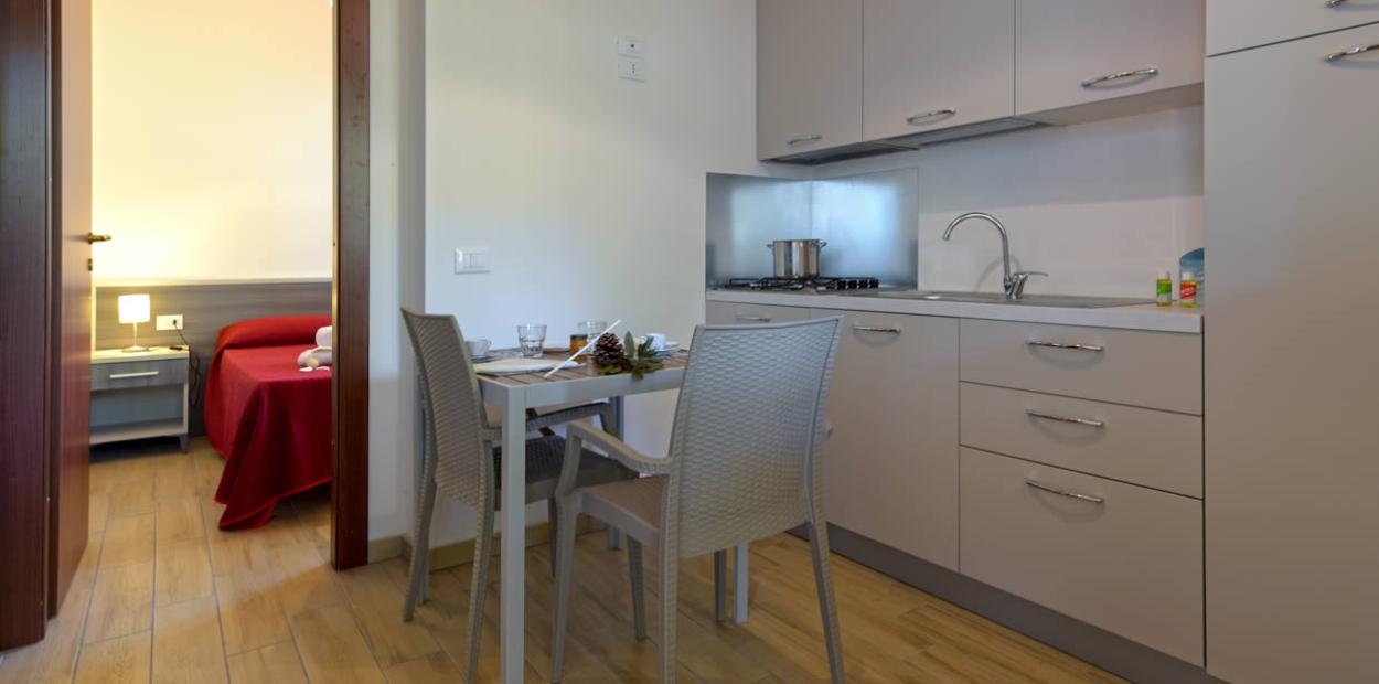 Cucina moderna con tavolo, sedie e accesso a camera da letto con letto rosso.