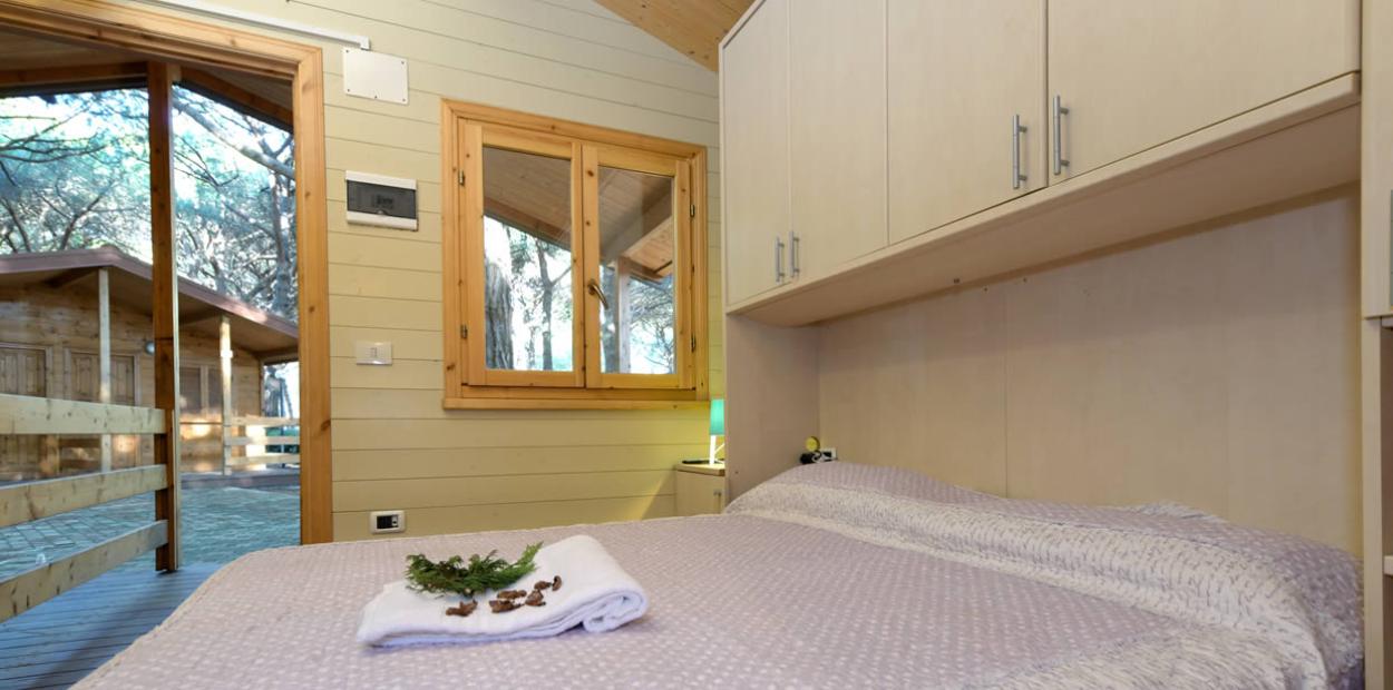 Camera accogliente in legno con letto, finestra e vista su una veranda.