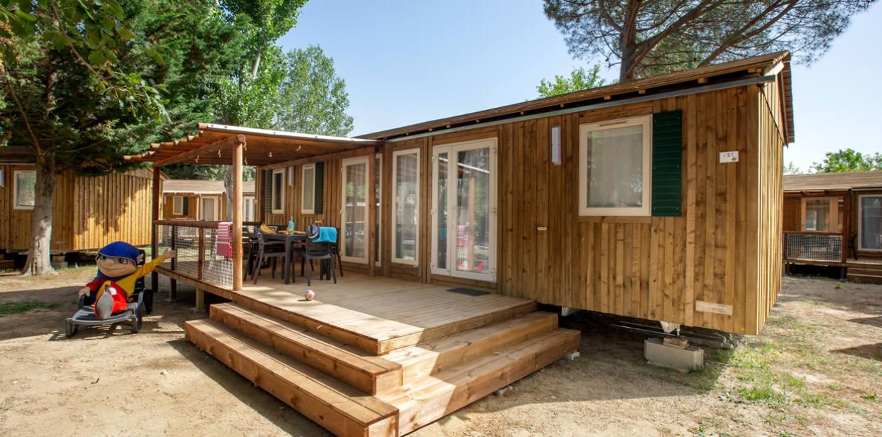 Bungalow in legno con veranda, sedie e tavolo all'aperto, circondato da alberi.