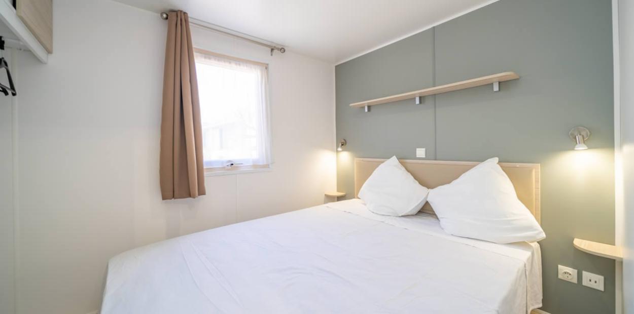 Camera da letto minimalista con letto matrimoniale, luci soffuse e tende beige.