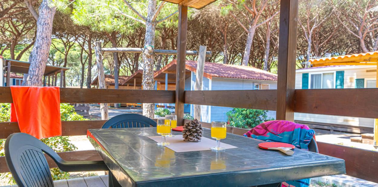 Veranda con tavolo, bevande e vista su bungalow tra gli alberi.