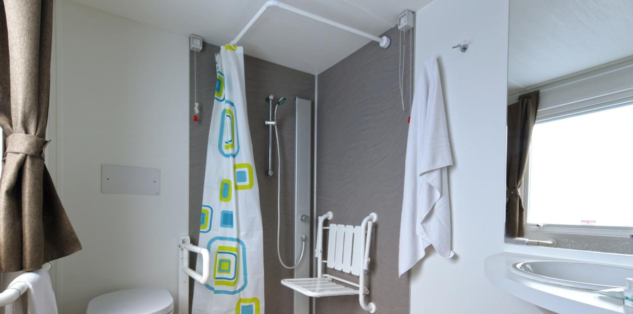 Bagno accessibile con doccia, sedile pieghevole e maniglioni per supporto.