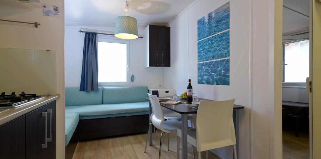 Moderno soggiorno con cucina, tavolo da pranzo e divano, illuminato da una finestra.
