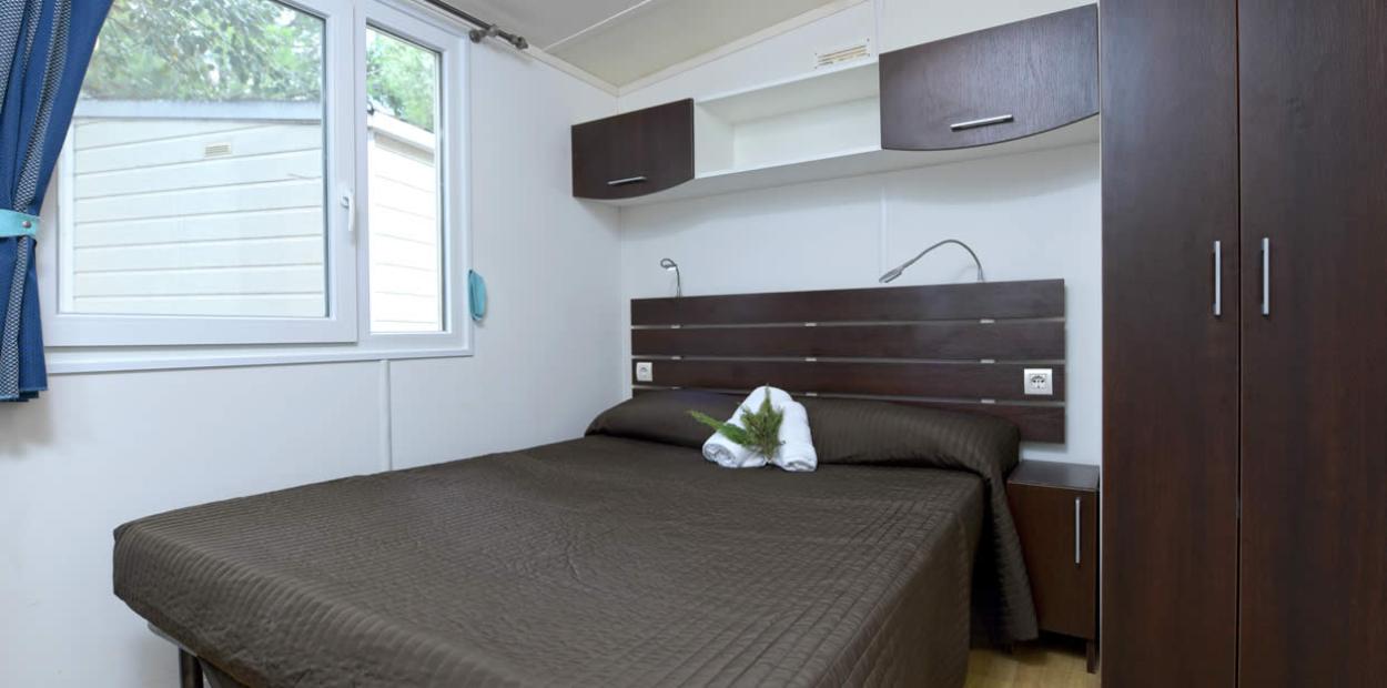 Camera moderna con letto matrimoniale, armadi scuri e finestra luminosa.