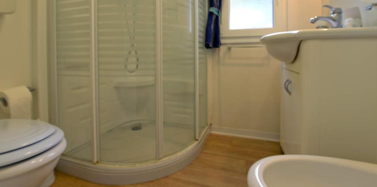 Bagno con doccia angolare, lavabo, WC e pavimento in legno chiaro.