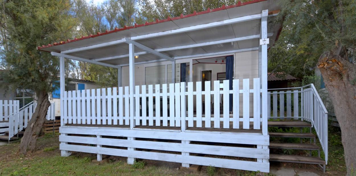 Veranda bianca in legno con staccionata, immersa nel verde, ingresso tramite scala.