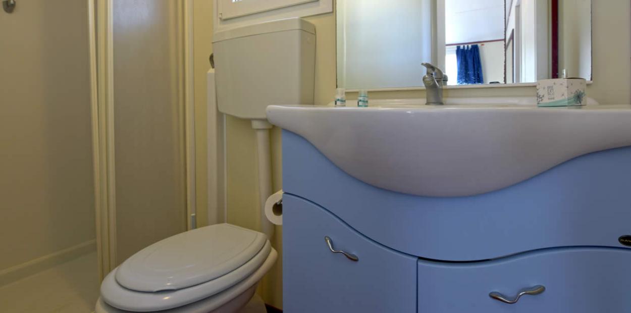 Bagno con sanitari bianchi e mobile lavabo azzurro, specchio sopra il lavandino.