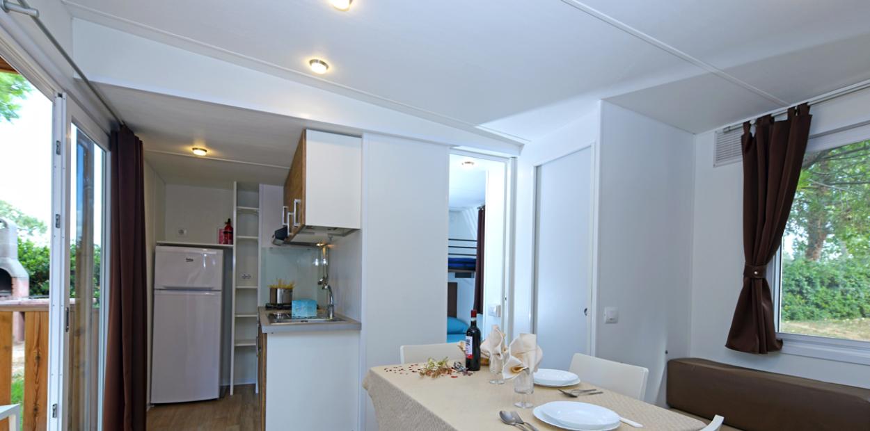 Interno di una casa mobile con cucina, tavolo apparecchiato e divano, vista esterna.