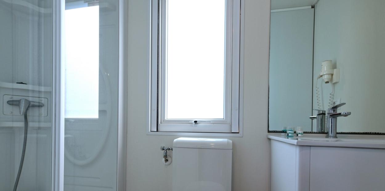 Bagno moderno con doccia, water, lavandino e finestra luminosa.