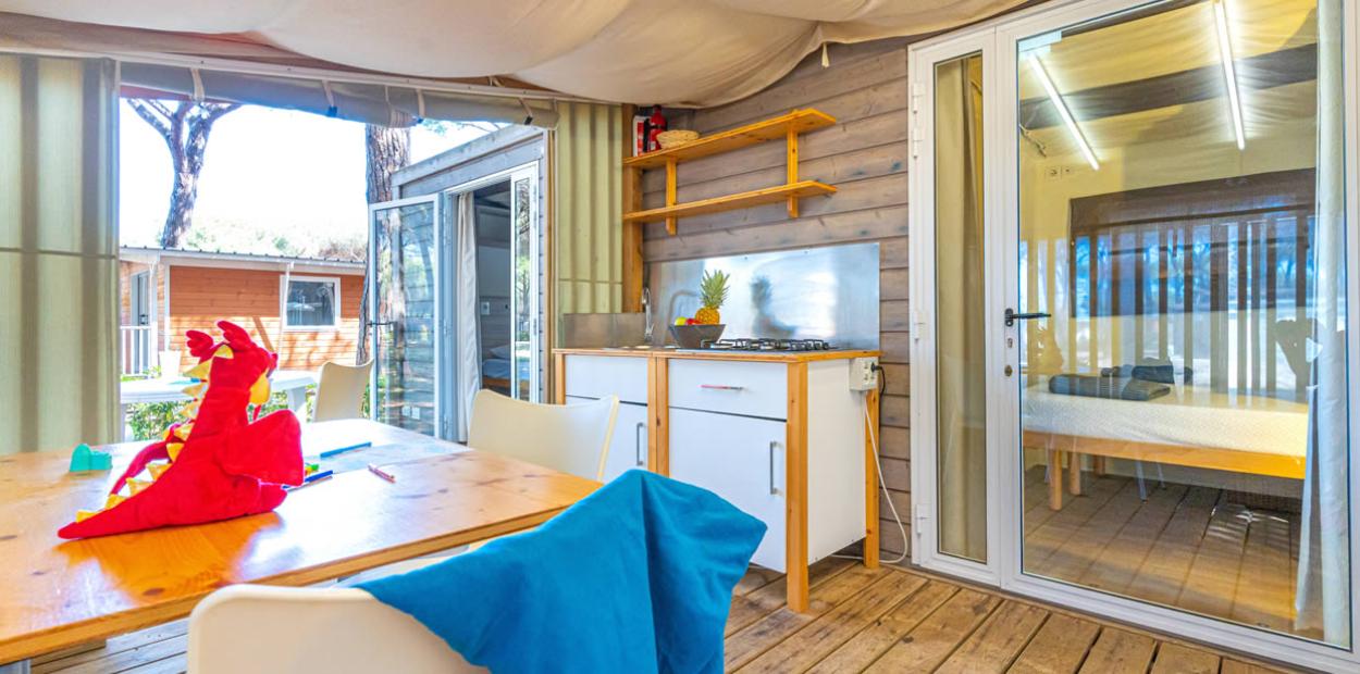 Interno accogliente con cucina, tavolo e giocattolo rosso, vista su bungalow esterno.