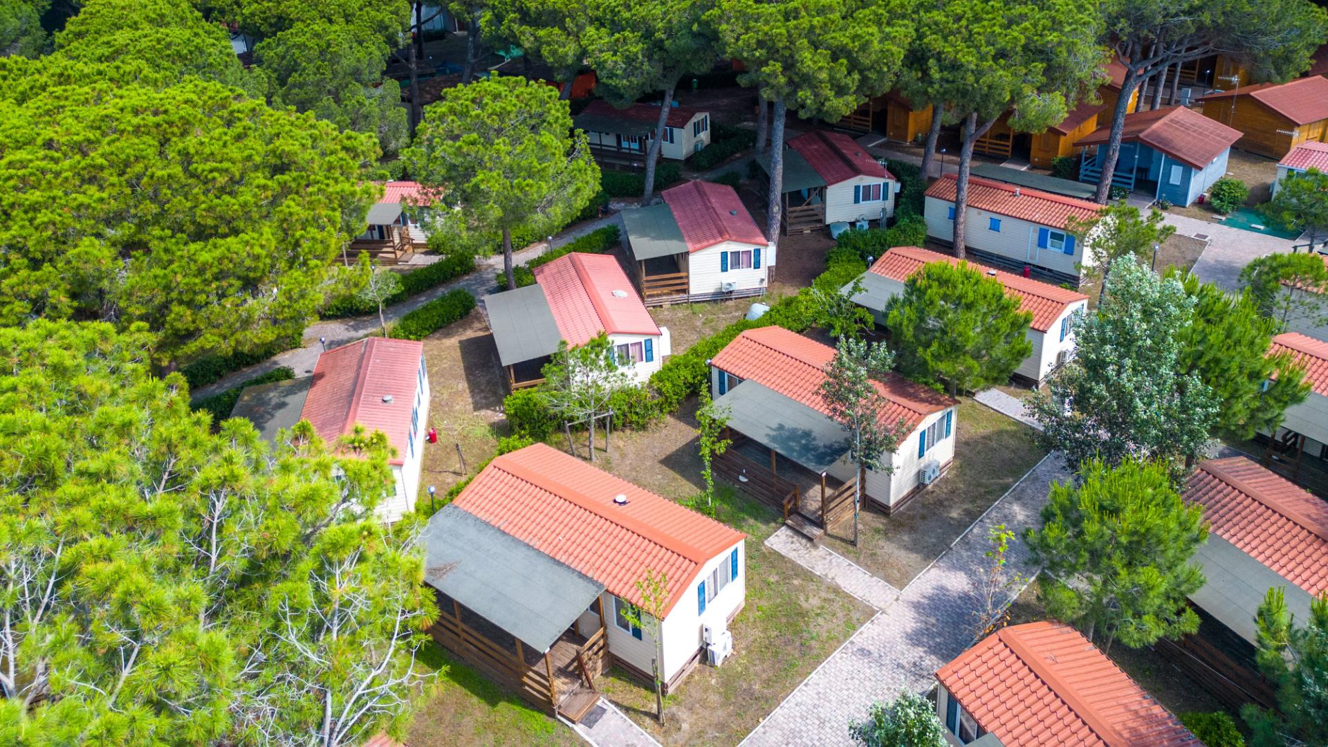 Villaggio turistico con bungalow tra alberi verdi e sentieri pavimentati.