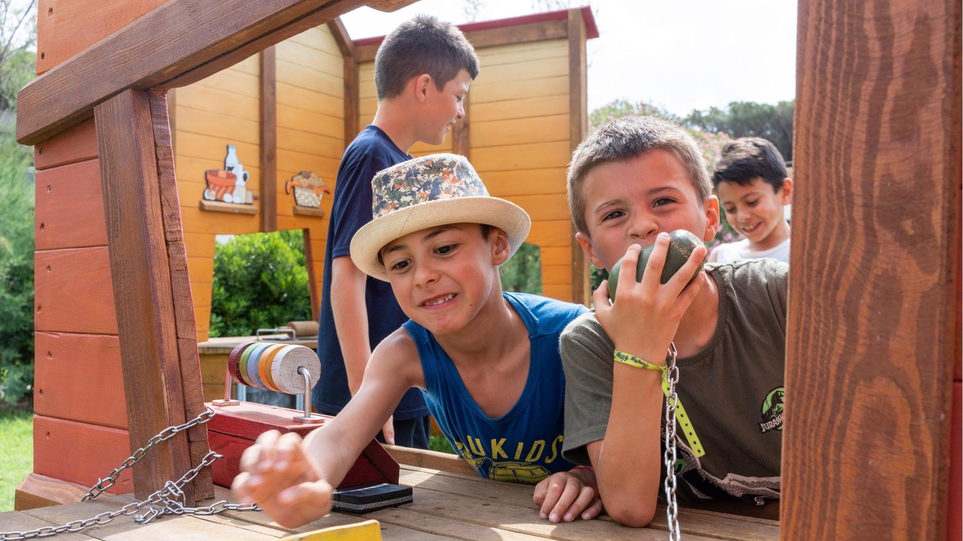 Bambini giocano in una casa di legno all'aperto, divertendosi con accessori colorati.