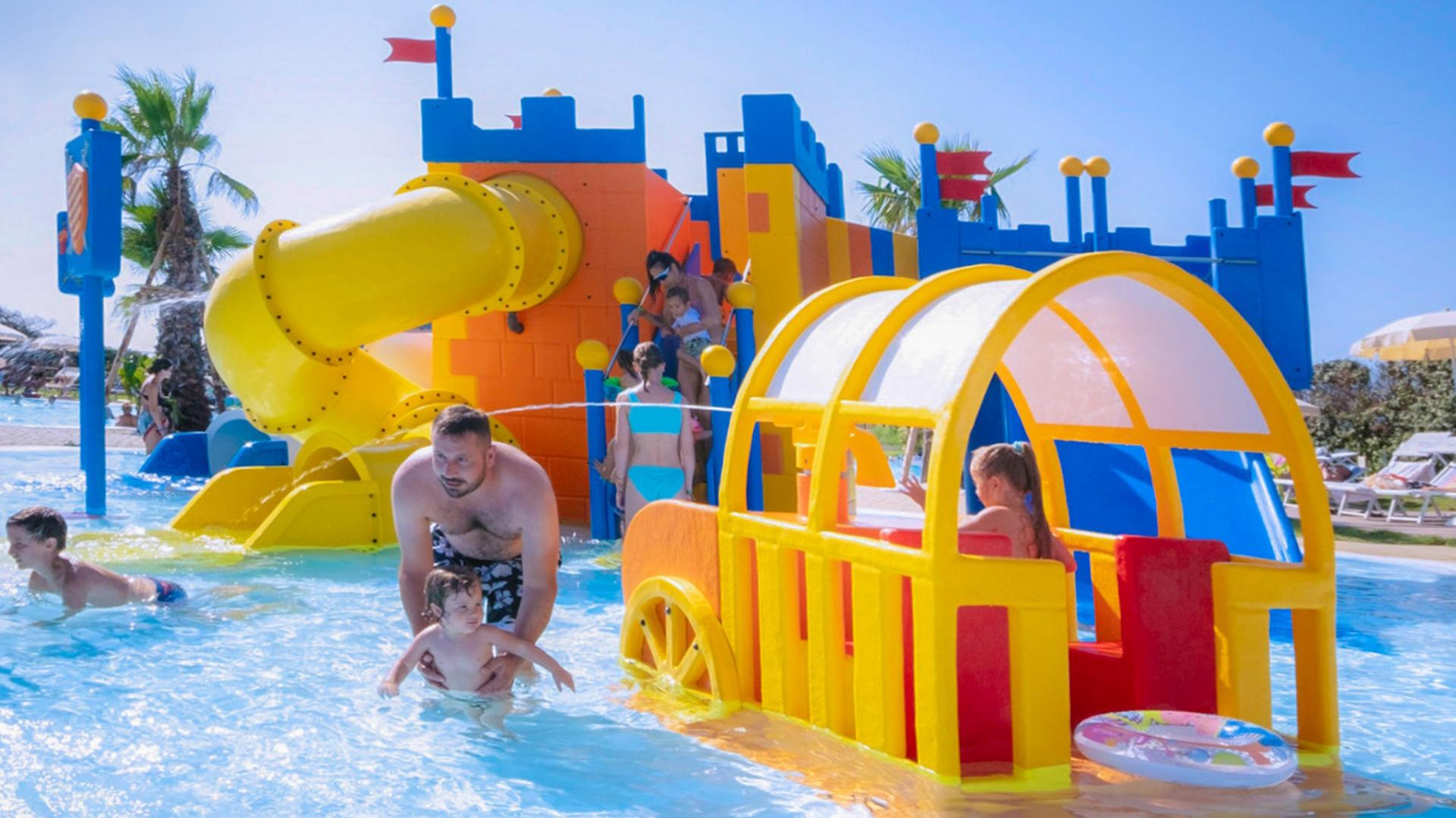 Parco acquatico con scivoli colorati e bambini che giocano in piscina.