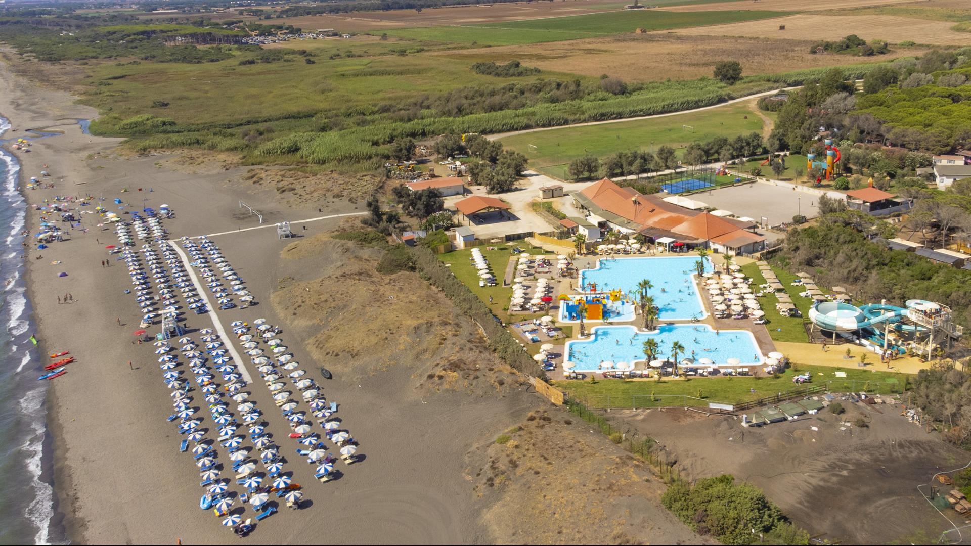 Spiaggia con ombrelloni chiusi, mare calmo e sole brillante all'orizzonte.