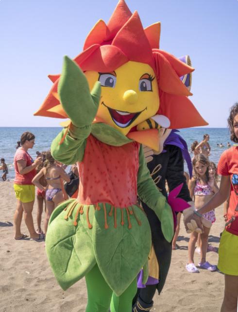 Costume da fiore colorato sulla spiaggia, circondato da bambini e bagnanti.