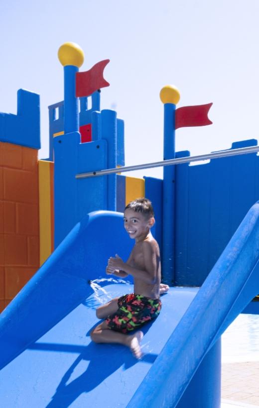 Bambino felice su uno scivolo blu in un parco acquatico colorato.