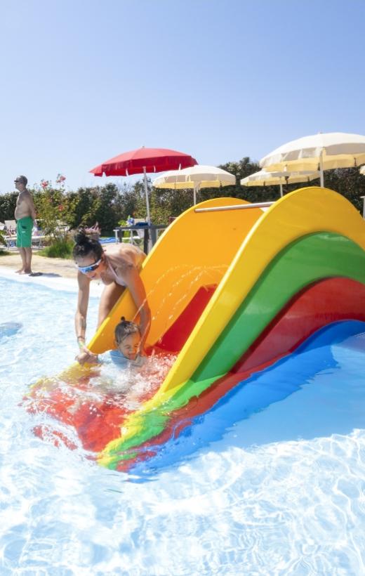 Bambina scivola sull'acqua con l'aiuto di un adulto in piscina colorata.