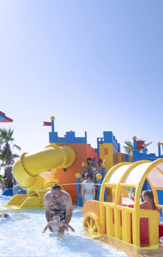 Bambino in piscina con scivolo, fa il segno di pace.