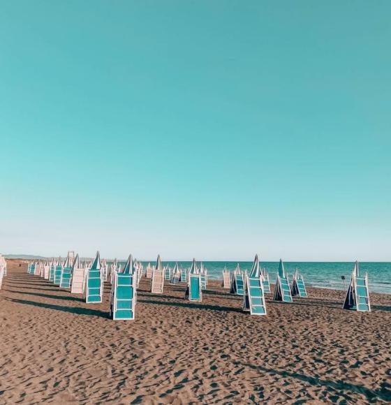 Spiaggia affollata con ombrelloni colorati, persone rilassate sotto il sole estivo.
