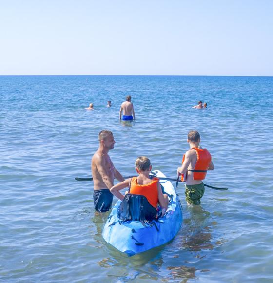 Spiaggia affollata con pedalò colorati e ombrelloni variopinti lungo la riva del mare.