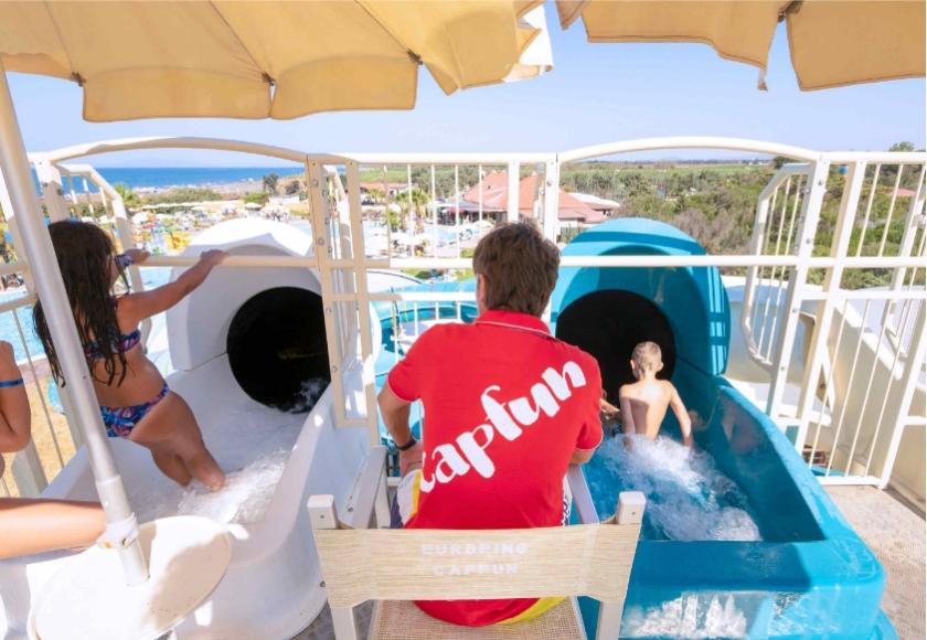 Scivoli d'acqua con bambini e supervisore in un parco acquatico soleggiato.