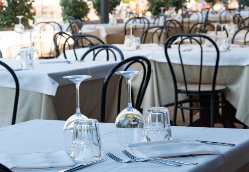 Ristorante elegante con tavoli apparecchiati, bicchieri rovesciati e sedie nere in ferro battuto.